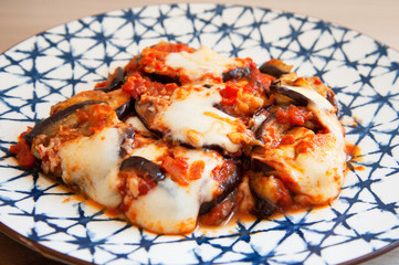 Parmigiana eggplants on ceramic vintage dish. Italian recipe: grilled aubergines, tomato sauce, mozzarella, parmigiano, basil, olive oil. Healthy food, non fried aubergines. Mediterranean diet.