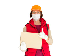 Fototapeta na wymiar Delivery service. A worker in a white mask and gloves, in a red vest and cap, brings a cardboard box, showing a thumbs up - that's good! 2020-nkovsky concept of the service of the pandemic coronavirus