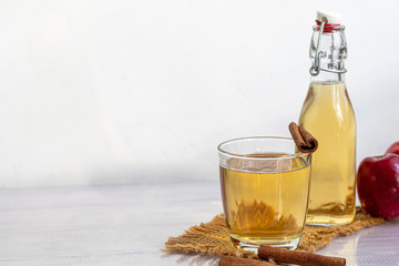Healthy organic foods. Apple cider in a glass bowl and fresh red apples on a light background. In a glass of ice cubes and nearby cinnamon sticks.