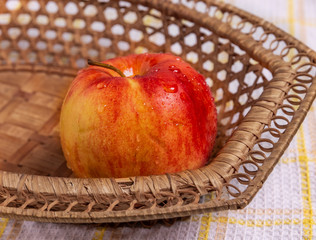A red Apple in a basket on the table. Drops of water glisten on the Apple.