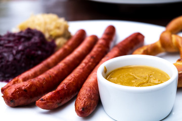 classic German snacks, sausages with mustard cabbage and bagel on a white plate