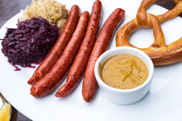 classic German snacks, sausages with mustard cabbage and bagel on a white plate