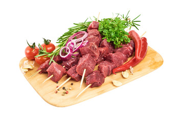 Meat skewers on bamboo skewers, with young basil, rosemary, red pepper, garlic and cherry tomatoes lie on a cutting board on a white background.