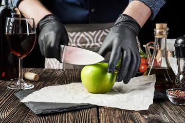 A man is cutting a ripe green apple that is lying on a stone chopping board on an old village...