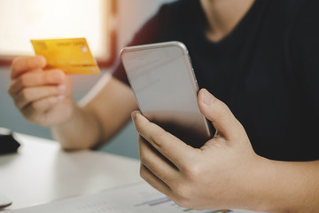 young man entering holding mobile phone and paying with mock up credit card on desk at home office, digital marketing, shopping online, electronic pay, online payment and digital technology concept