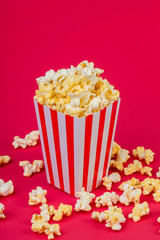 Paper cup with popcorn on color background. Striped box with popcorn on red background.Popcorn in red and white striped cardboard bucket .