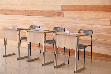 Modern school desks near wooden wall