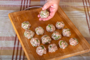 Female hands lay raw homemade meatballs from fresh minced meat with greens on a kitchen board