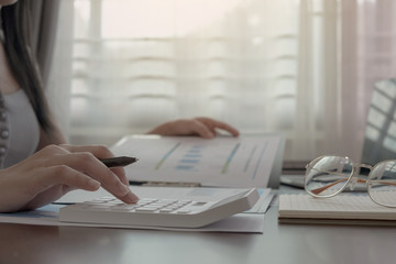 Close up of woman or accountant hand holding pen working on calculator to calculate business data, accountancy document and laptop computer at work for home. business concept