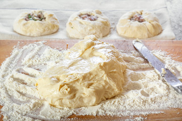 Fresh raw yeast dough on a wooden board with flour on a background of raw pies with meat filling. Close-up
