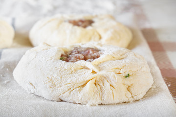 Raw dough with meat filling on a table with flour. Close-up