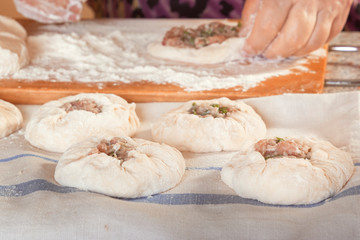 Raw dough with meat filling on the table against the background of female hands with pieces of dough.