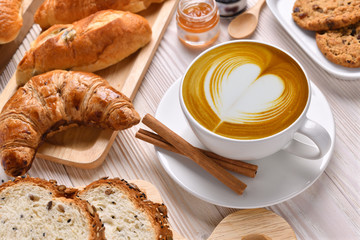 Fototapety  Widok z góry na filiżankę kawy latte z pieczywem lub bułką, rogalikiem i piekarnią na białym drewnianym stole