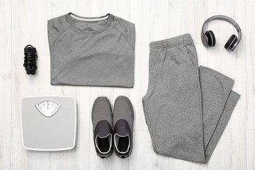 Composition with sportswear and weight scales on wooden background