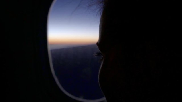 Slow motion shot of young woman looking airplane through during sunset, close-up of thoughtful female passenger - New York City, New York
