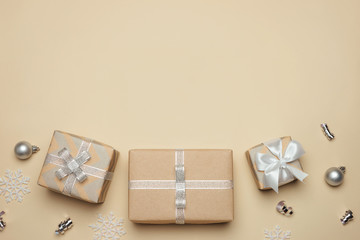 Obraz na płótnie Canvas Gift boxes wrapped in kraft paper with silver ribbon and bow on pastel beige background. Winter holidays present concept. Christmas background, festive decor. Top view with free space. Flat lay. 