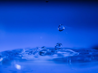 Water drop creating waves ripples and air borne water droplet