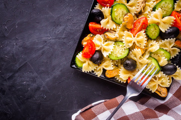 tasty pasta salad with tomato cucumber and olives on a dark stone background