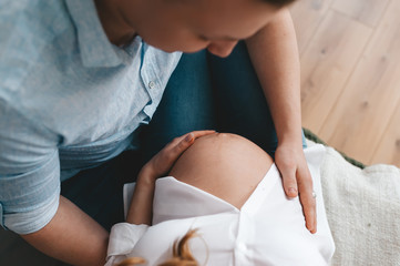 Couple's hand on pregnant mother belly indoors. Top view