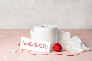 Toilet paper with red thread on color table. Hemorrhoids concept