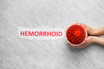 Female hands with cactus and word HEMORRHOID on light background
