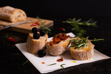 Sliced bread with olive oil, black olives, tomatoes and rosemary.  Mediterranean typical food. Black background.