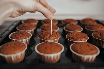 Chocolate muffins bakery. Brownie cupcakes on the baking pan. Baking at home, home bakery. Woman cheсks muffins with toothpick.