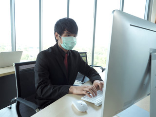 Asian business man or employee wear medical mask is working on his computer desktop.Office personal...
