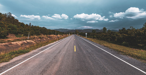 Empty asphalt road through the green field and clouds on blue sky in summer day.
