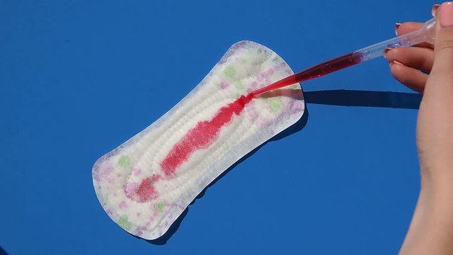 A girl pours red water like blood on a menstrual sanitary pad. Leakage protection concept, close-up,