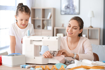 Little daughter with her mother sewing protective masks at home