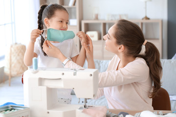 Little daughter with her mother sewing protective masks at home