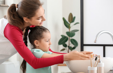 Little daughter with her mother washing hands in bathroom
