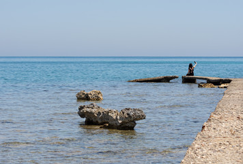 Fototapeta premium A woman sitting on the rock looking sea and taking photo