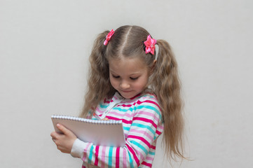 A portrait of a fair-haired schoolgirl stands with a notebook in her hands and writes in it. Light grey Studio background. Education. copy place