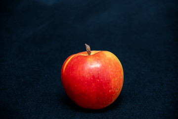 One ripe fresh organic sweet red apple with yellow spots, close-up, on a blue jeans background trendy color, color 2020