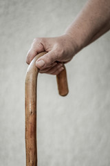 Closeup of senior woman's hand on wooden walking stick. Selective focus on fingers, black and white.
