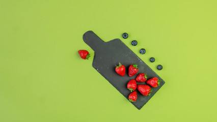 Fresh berries on black stone board. Strawberries and blueberries on black kitchen board and solid green background. Fresh berries concept with copy space.