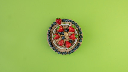 Bowl of muesli with with fresh strawberries and blueberries on solid green background. Healthy breakfast concept. Vege meals concept. 