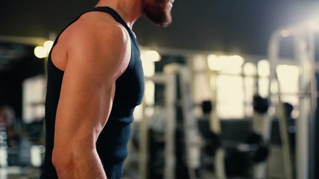 Close-up of unrecognizable athletic young man with muscular wiry body wearing sportswear doing weight lifting during sport workout training in modern dark gym. Tracking shot in slow motion.