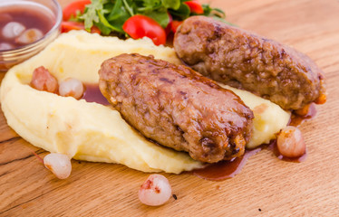 A dish of meat cutlets, mashed potatoes, fresh vegetables and sauce on a wooden board on a white background