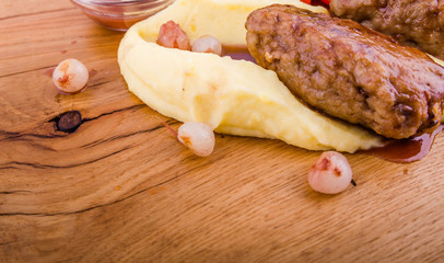 A dish of meat cutlets, mashed potatoes, fresh vegetables and sauce on a wooden board on a white background