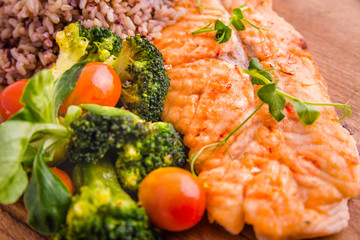 Golden grilled fish fillet with a side dish of rice and vegetables on a wooden board on a white background