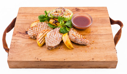 Grilled pieces of pork, apples and zucchini on a wooden board on a white background