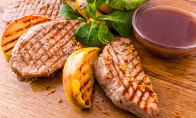 Grilled pieces of pork, apples and zucchini on a wooden board on a white background