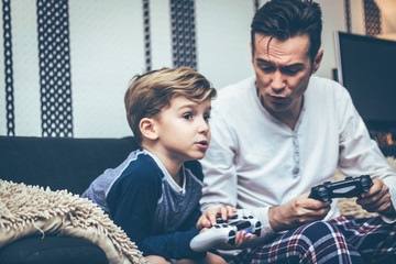 Father and son talking while playing video games at home.