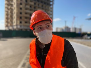 Portrait of male construction worker in medical mask and overalls on background of house under construction.