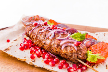 Kebab, meat on a skewer, pita bread, side dish of onions and tomatoes, pomegranate seeds and sauce on a wooden board