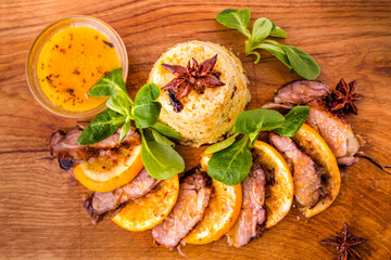 Juicy stewed duck breast in the company of turmeric with prunes, dried apricots and orange sauce on a wooden board