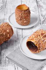 Trdelnik covered in nuts and sugar with chocolate inside against white wooden background. Czech street food